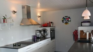 Une cuisine moderne avec des meubles blancs, une hotte de cuisinière en acier inoxydable, une machine à café et une horloge ronde au mur.