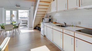 A modern kitchen with white cabinets, a wooden staircase, and a dining area with a view.