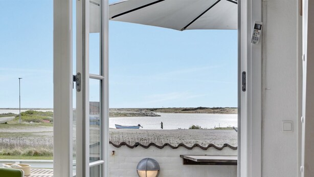 A room with a view of a beach, a small boat, and a lamp on the wall.