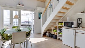 A modern kitchen with a wooden staircase, a dining area with a table and chairs, and a view of the sea through large windows.