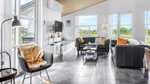 Un salon moderne avec un plafond en bois, de grandes fenêtres, un téléviseur à écran plat et un coin salon confortable avec un fauteuil en fourrure et deux canapés.