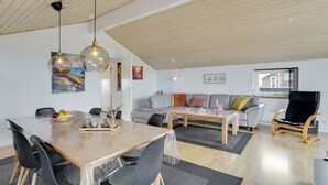 Un salon moderne avec un coin repas, un plafond en bois et des œuvres d’art accrochées aux murs.