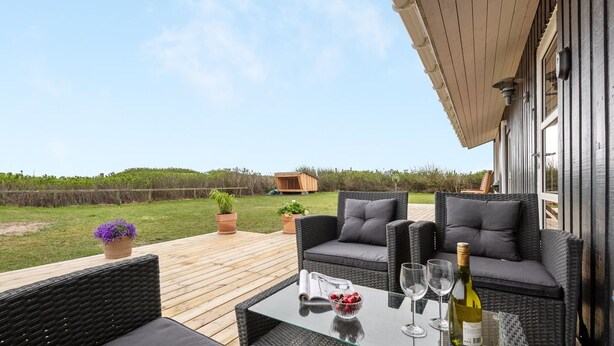 An outdoor patio area with wicker furniture, a glass table, and potted plants. - "Thamara" - 350m from the sea by Interhome (Harboøre)