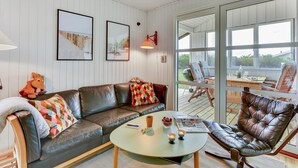 A cozy living room with a leather sofa, a coffee table, and a leather armchair. There are framed pictures on the wall and a large window offering a view of the outdoors. - "Thamara" - 350m from the sea by Interhome (Harboøre)