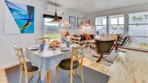 A dining area with a table set for four, surrounded by wooden chairs. There is a sofa with cushions and a coffee table in the background. - "Thamara" - 350m from the sea by Interhome (Harboøre)