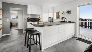 Una cocina moderna con una isla grande, armarios blancos y vistas al exterior.