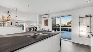 Cocina moderna con una isla grande, electrodomésticos de acero inoxidable, iluminación colgante y vistas al exterior.