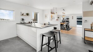 Una cocina moderna con una isla grande, un comedor con mesa y sillas de madera, y vistas al exterior.