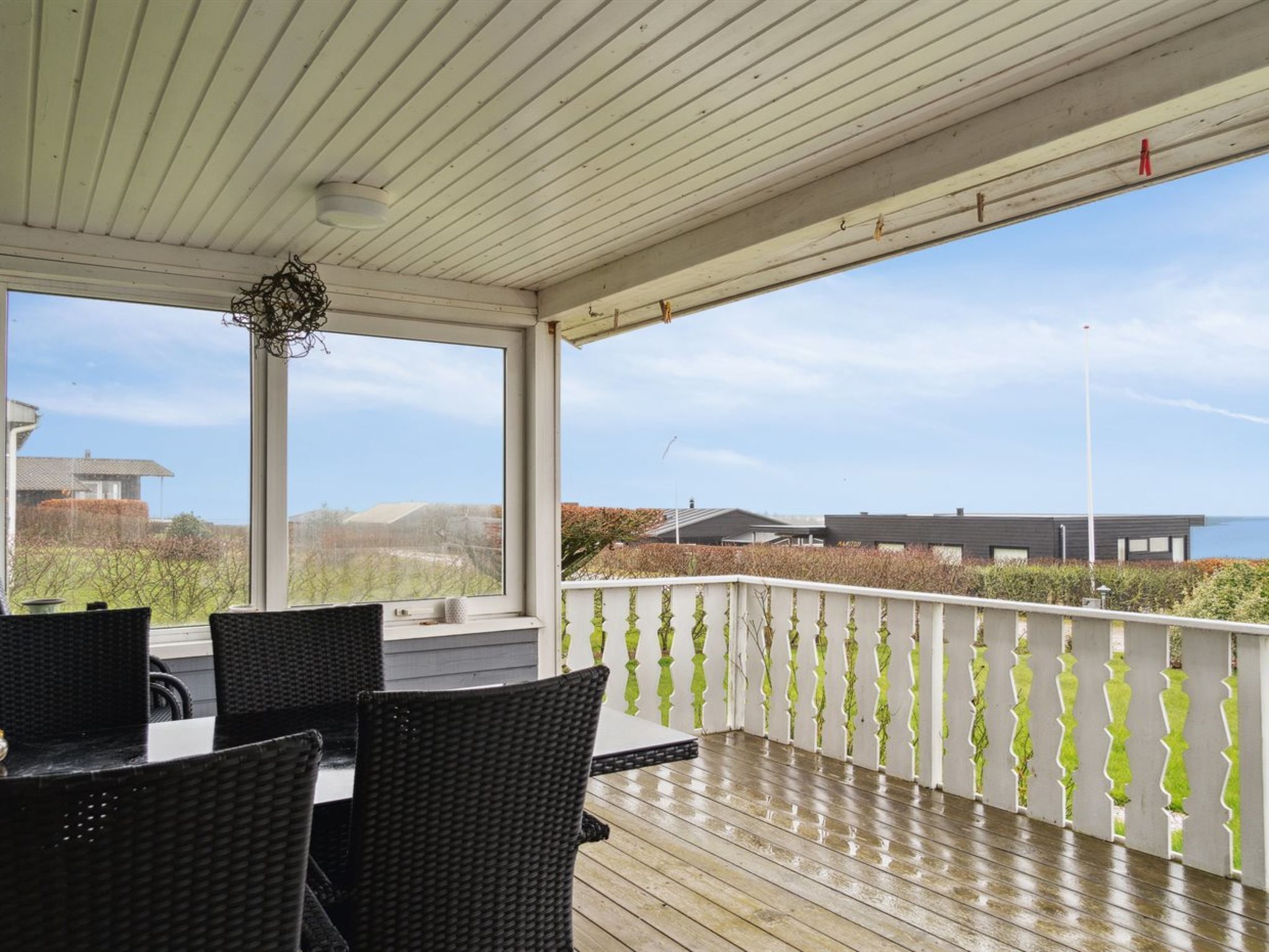 A covered outdoor area with a wooden deck, wicker furniture, and a view of the sea and buildings in the background.