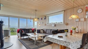 A spacious living area with a wooden ceiling, large windows, a sofa set, a dining table, and a view of the outdoors. - "Ormar" - 100m to the fjord by Interhome (Lemvig)