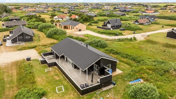 Ein modernes Haus mit einer großen Terrasse, einem Trampolin und einem gepflegten Rasen.
