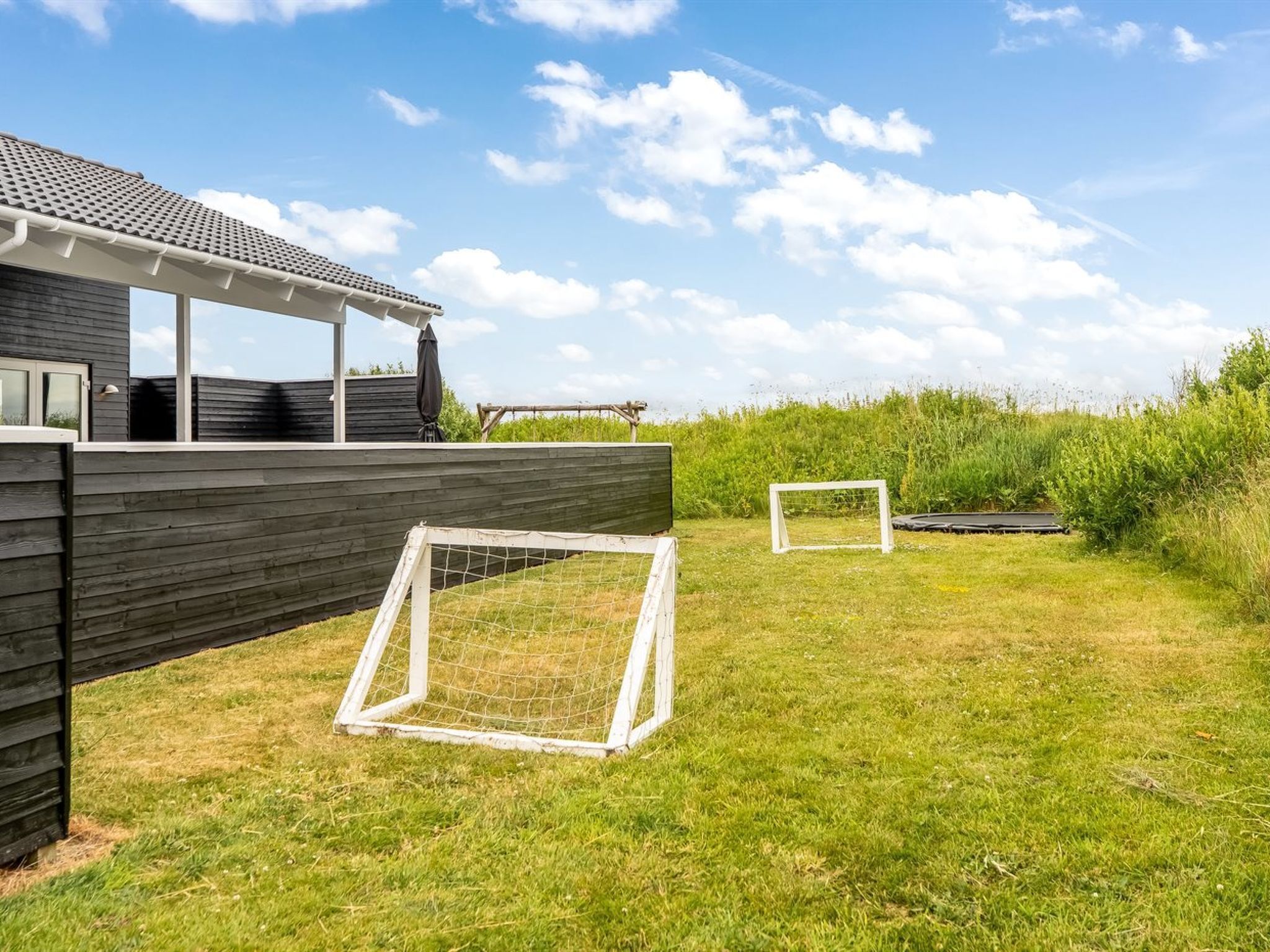 Une maison moderne dotée d’un patio couvert, d’une pelouse et de deux buts de football.