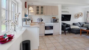 Eine moderne Küche mit einer zentralen Kochinsel, einem Essbereich mit grauem Sofa und einem an der Wand montierten Fernseher.