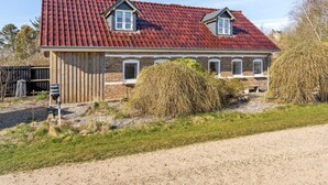 Ein zweigeschossiges Haus mit rotem Ziegeldach, einem Holzschuppen und einem Schotterweg.