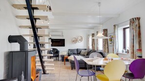 Ein modernes Wohnzimmer mit Kamin, einer Essecke mit bunten Stühlen, einer Couch und einer Treppe mit Holzwangen.