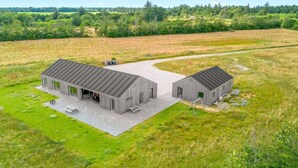 Een modern gebouw met een plat dak en grote ramen, omgeven door een grasveld en bomen.