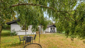 A backyard with a swing set, a dining table with chairs, and a house with a covered patio.