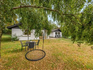A backyard with a swing set, a dining table with chairs, and a house with a covered patio.