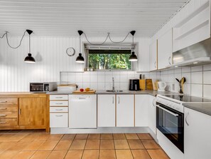 Una cocina moderna con armarios blancos, lavavajillas, estufa y ventana con vistas a zonas verdes.