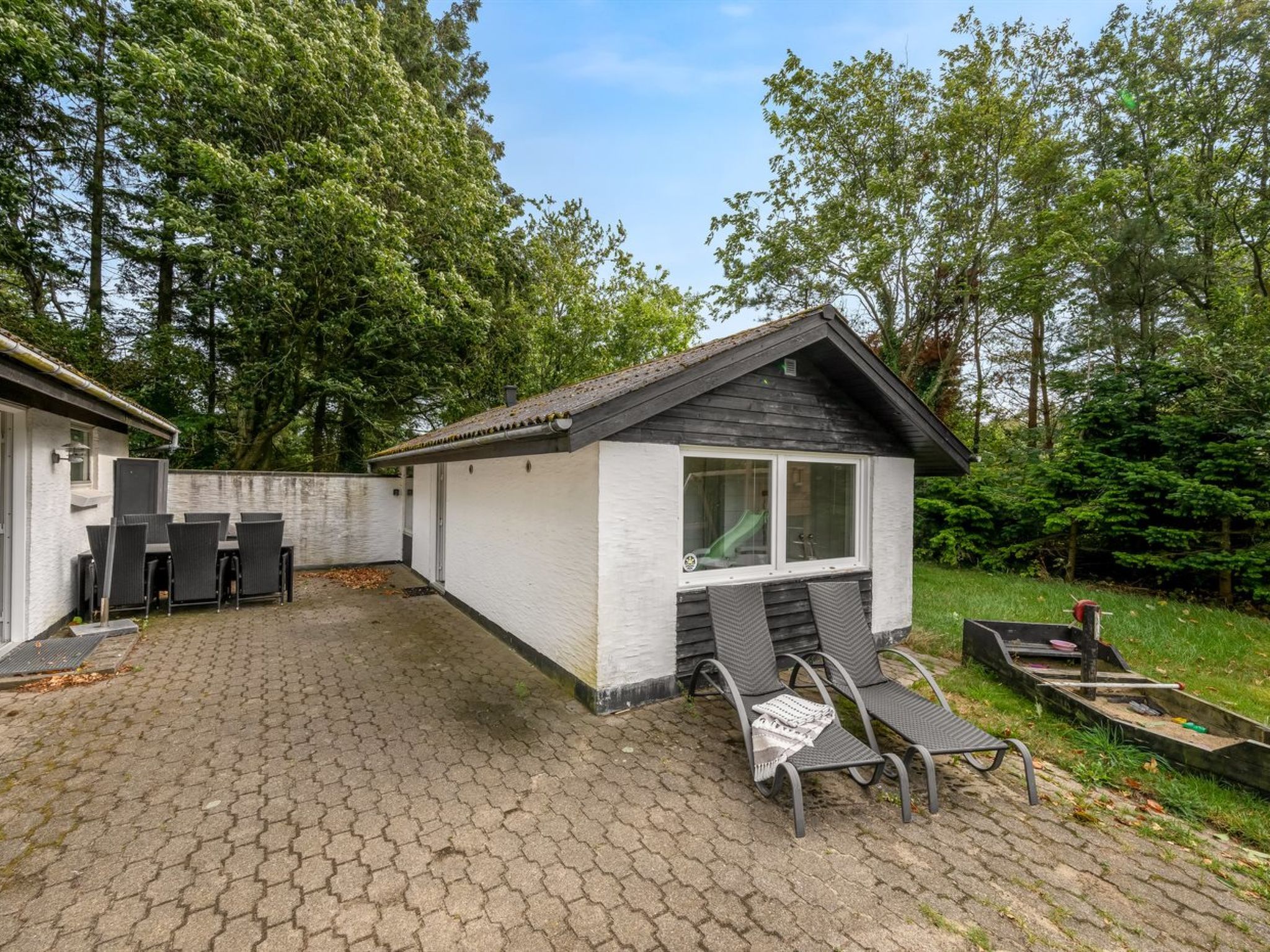 Ein kleines, eingeschossiges Gebäude mit einer Terrassenfläche, belegt mit sechseckigem Pflaster, Sitzgelegenheiten im Freien und einem kleinen Boot.
