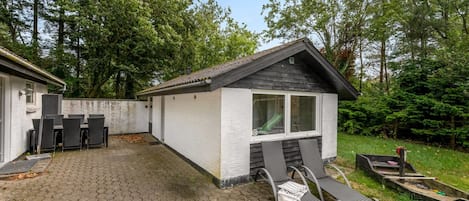 Ein kleines, eingeschossiges Gebäude mit einer Terrassenfläche, belegt mit sechseckigem Pflaster, Sitzgelegenheiten im Freien und einem kleinen Boot.