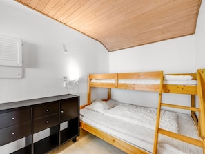 A bunk bed with white bedding, a dark wooden dresser with drawers, and a ceiling with wooden beams.