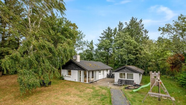 A two-story house with a patio and a swing set in a wooded area.