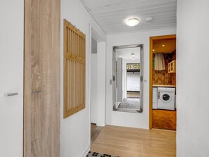 Un pasillo con piso de madera, una puerta blanca y vista a un cuarto con lavadora.