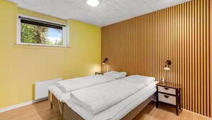 A bedroom with two beds, a window, a radiator, and a wooden panel wall.