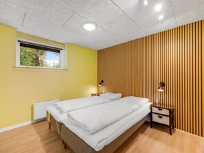 A bedroom with two beds, a window, a radiator, and a wooden panel wall.