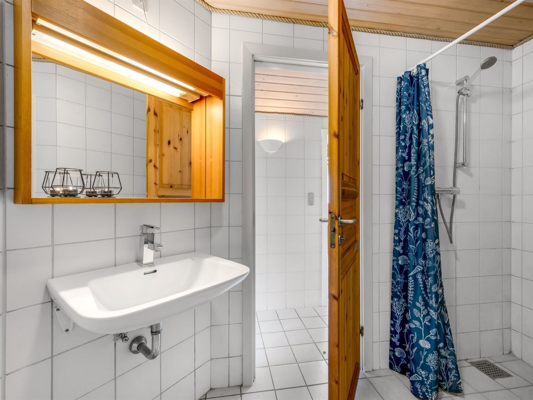 Un baño con un lavamanos blanco, un espejo y una ducha con cortina de baño estampada con motivos florales azules.