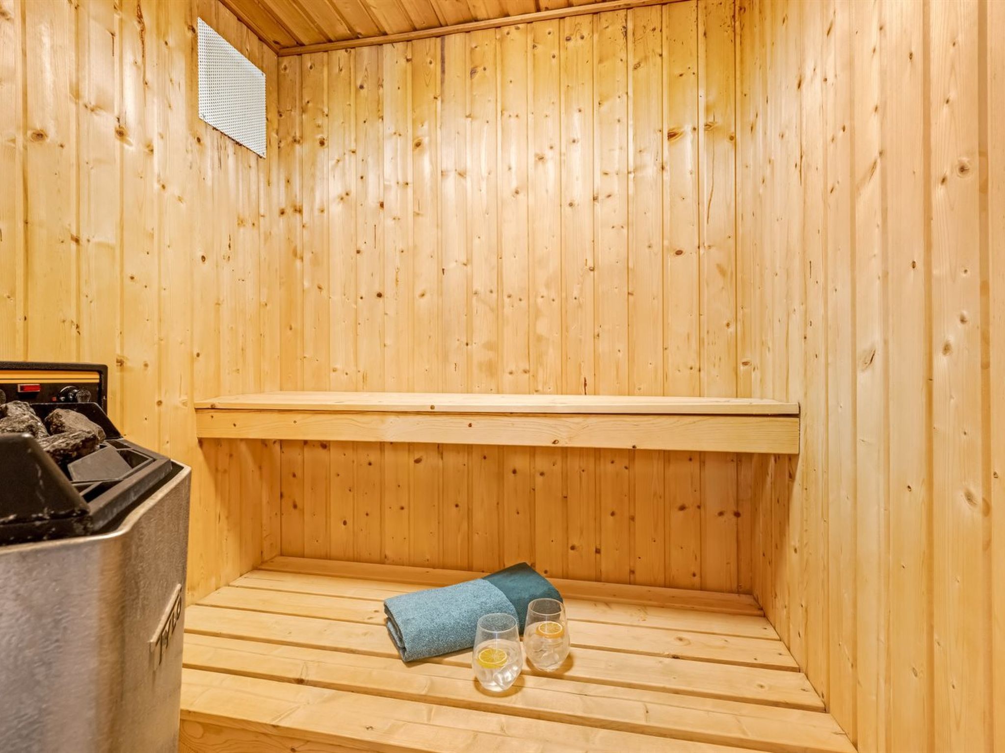 A sauna room with wooden walls, a bench, a heater, and two glasses with lemon slices.