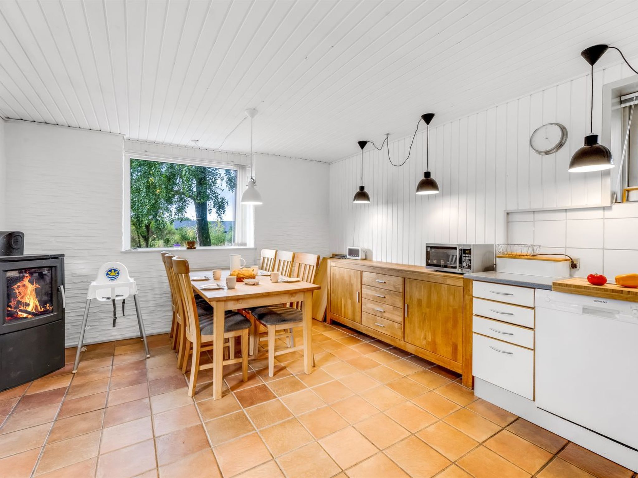 Eine moderne Küche mit weißen Schränken, einem Essbereich mit Holzsesseln und einem sichtbaren Kaminofen.
