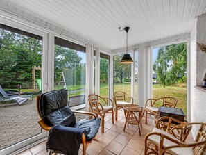 A sunlit room with large windows, wicker furniture, and a view of a garden.