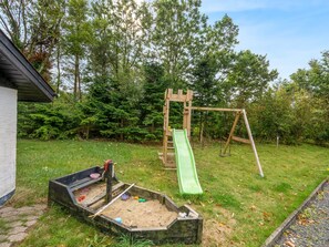 Un parque infantil con tobogán y columpios, rodeado de árboles.