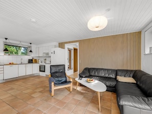 A modern living space with a kitchen, a black leather sofa, a wooden chair, and a dining table.