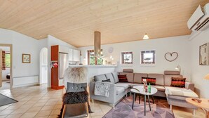 Un'ampia zona giorno con soffitto in legno, un divano grigio, un piccolo tavolino rotondo e un tappeto decorato.
