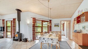 Un'ampia zona giorno con soffitto in legno, un camino, un tavolo da pranzo con sedie e un angolo cottura con pensili in legno.