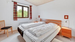 Camera da letto con due letti, una sedia di legno, un comodino e una finestra con tende.