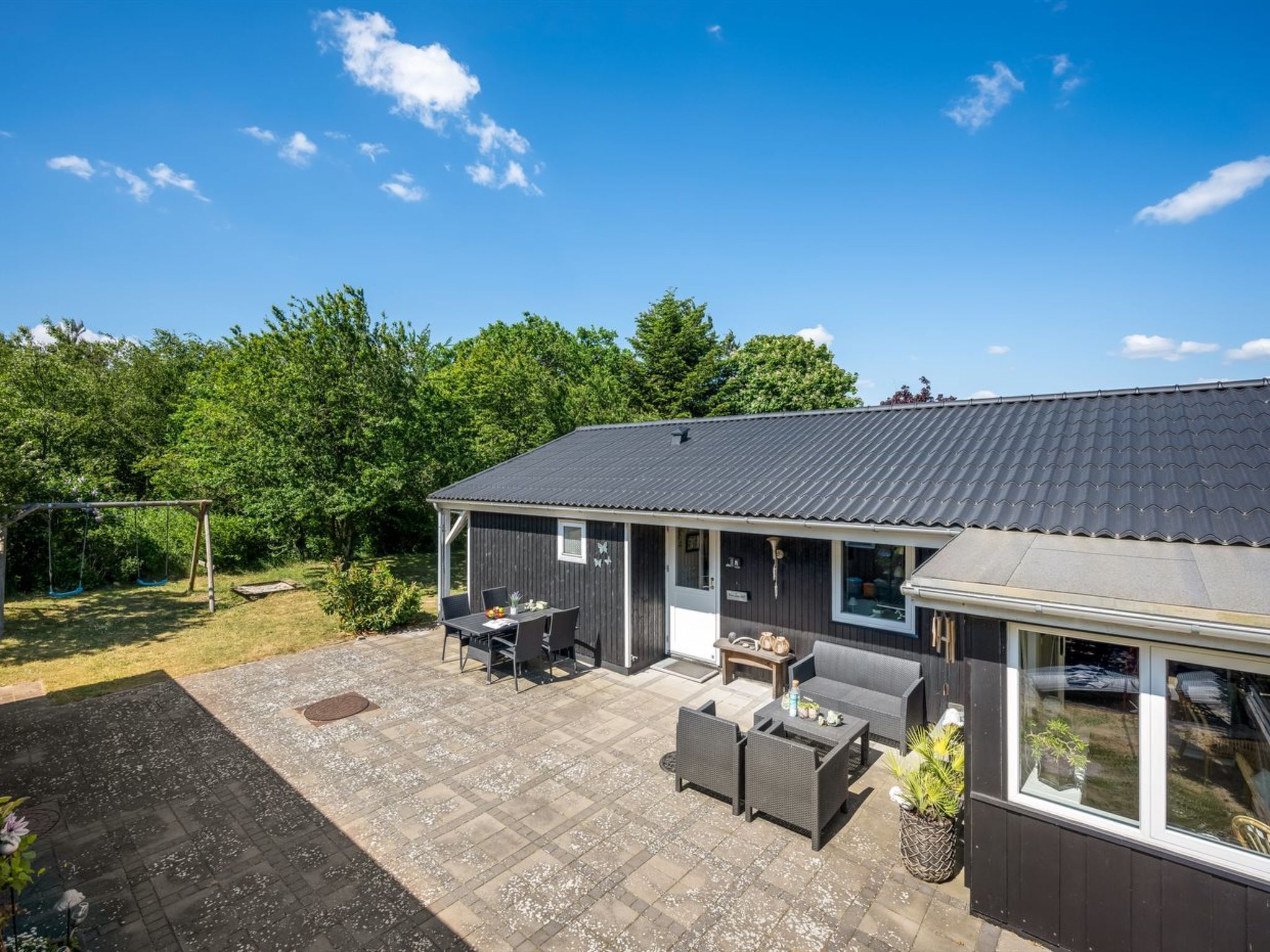 Een modern huis met een terras, straatmeubilair en een schommel.
