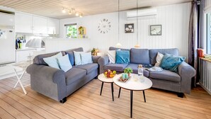 En moderne stue med en grå sofa, et sofabord og et køkken i baggrunden.