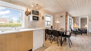 Una cocina moderna con armarios de madera, un comedor con sillas negras y vistas al exterior.