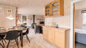 Una habitación acogedora con techo de madera, un comedor con mesa y sillas, una cocina con armarios de madera y una cama junto a una ventana.
