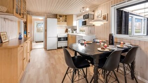 Una cocina moderna con armarios de madera, una isla central y un comedor con sillas negras.