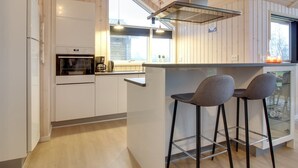 A modern kitchen with white cabinetry, a built-in oven, a coffee maker, and a bar area with two stools. - "Gertrude" - 1.1km to the fjord by Interhome (Hemmet)