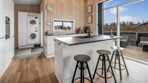 Une cuisine moderne avec un lambris en bois, une grande fenêtre et un coin bar avec des tabourets.