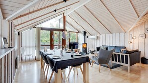 Un loft spacieux avec de hauts plafonds, des poutres apparentes, un coin repas avec une longue table et un coin salon confortable doté d’une cheminée.