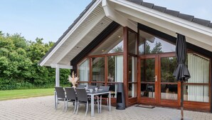 Une maison moderne dotée d’un patio comprenant une table et des chaises, de grandes portes vitrées et un espace salon abrité.