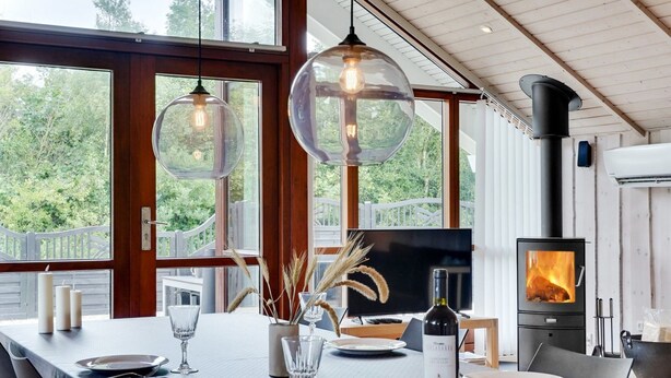 Un espace repas moderne avec une longue table dress ée pour deux personnes, une cheminée et de grandes fenêtres offrant une vue sur l’extérieur.