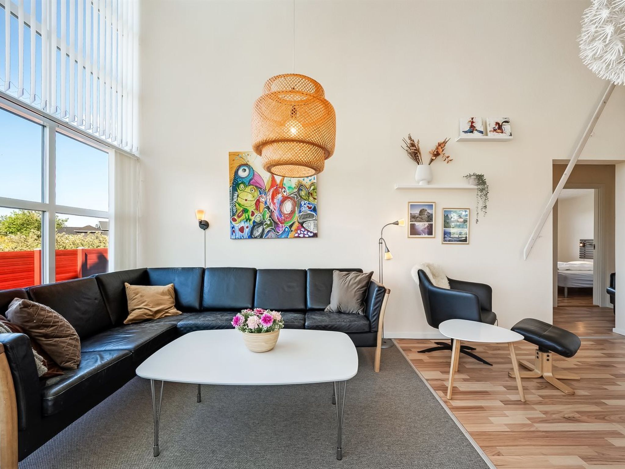 Un salon moderne avec un canapé en cuir noir, une table basse blanche et un tableau abstrait aux couleurs vives.